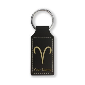 May include: Black leather keychain with a gold Aries zodiac symbol and the text "Your Name" engraved on it.