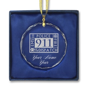 May include: A clear crystal ornament with a blue and white 911 dispatch logo, the words "Police, Fire, EMS" and the text "Your Name Year". The ornament is in a blue velvet box.