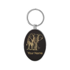 May include: A black oval keychain with a gold outline features a detailed line drawing of an elephant. The keychain has a silver ring and the text "Your Name" is printed in gold below the elephant.