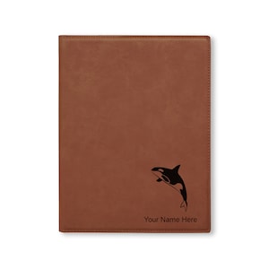 May include: A brown leather-bound journal with an engraved image of an orca jumping out of the water. The text "Your Name Here" is engraved below the orca.