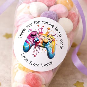 May include: A cellophane bag filled with colourful marshmallows, tied with a purple ribbon. A round sticker on the bag features a vibrant, watercolour-style video game controller with the text "Thank you for coming to my party. Love from Lucas."