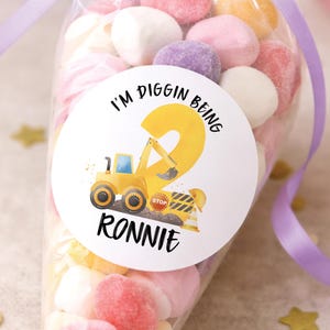 May include: A cellophane bag filled with colourful sweets, tied with a purple ribbon. A white circular sticker on the bag reads "I'm Diggin Being 2 Ronnie" with a yellow construction vehicle and number 2.