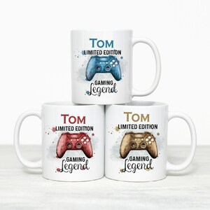 Op de afbeelding: Drie witte keramische mokken met een gaming controller afbeelding in aquarel-stijl in blauw, rood of bruin. Elke mok toont de naam Tom, de tekst Limited Edition en het woord Gaming Legend in een sierlijk lettertype met kleurrijke verfspatten.