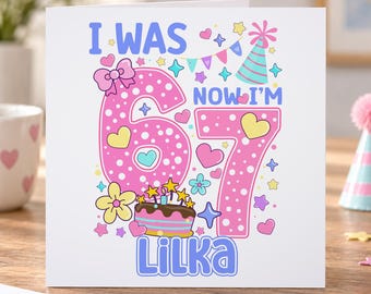 May include: A square greeting card featuring the text I WAS NOW I'M 67 LILKA in blue. The design includes a large pink polka-dot number 67, a birthday cake with lit candles, a party hat, colorful stars, hearts, flowers, and bunting.