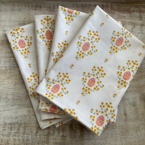 May include: Set of four white cotton napkins with a floral pattern featuring pink and yellow Easter eggs.