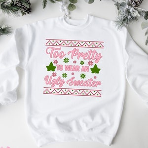May include: A white sweatshirt with a pink and green design that says "Too Pretty To Wear An Ugly Sweater".