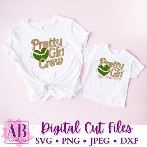 May include: Two white t-shirts with a pink and green design. The larger shirt says "Pretty Girl Crew" with a green heart and a string of pearls. The smaller shirt says "Pretty Girl In Training" with a green heart and a string of pearls.