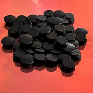 May include: A pile of black plastic snap fasteners. The fasteners are round and have a small hole in the center.