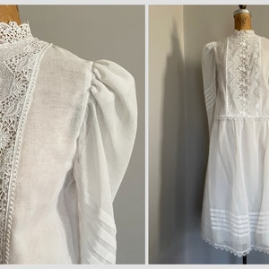 May include: White vintage dress with a high neck and long sleeves. The dress has a lace overlay on the bodice and a tiered skirt.