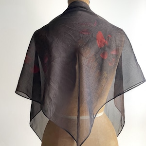 May include: A sheer black scarf with a red floral print. The scarf is draped over a mannequin.