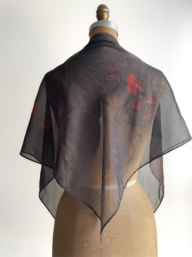 May include: A sheer black scarf with a red floral print. The scarf is draped over a mannequin.