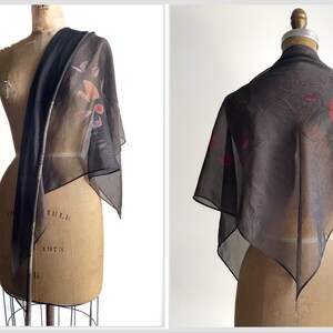 May include: A sheer black scarf with a floral print in shades of red, pink, and brown. The scarf is draped over a dress form.