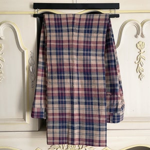 May include: A pair of plaid pants hanging on a hanger. The pants are a beige, red, and blue plaid pattern.