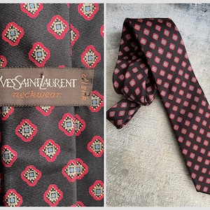 May include: A black silk tie with a red and blue geometric pattern. The tie has a brown label that reads "Yves Saint Laurent neckwear" and "silk".