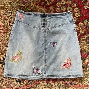 May include: A light blue denim skirt with embroidered butterflies in shades of pink, yellow, and green.