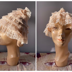 May include: A delicate, off-white lace hat with multiple ruffles. The hat is worn on a mannequin head.
