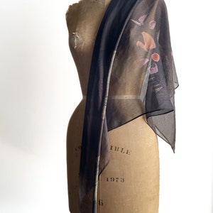 May include: A sheer black scarf with a colorful abstract print. The scarf is draped over a dress form.