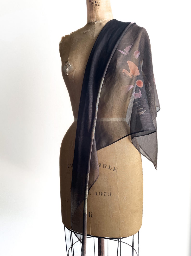May include: A sheer black scarf with a colorful abstract print. The scarf is draped over a dress form.