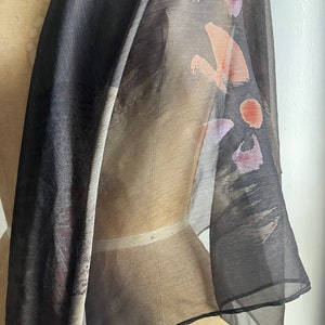 May include: A sheer black scarf with abstract brown, pink, and orange brushstrokes. The scarf is draped over a dress form.