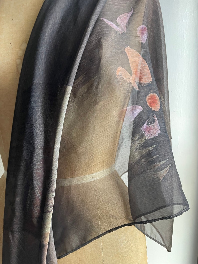 May include: A sheer black scarf with abstract brown, pink, and orange brushstrokes. The scarf is draped over a dress form.