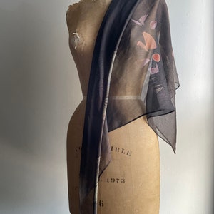 May include: A sheer black scarf with a brown, pink, and white abstract print. The scarf is draped over a dress form.