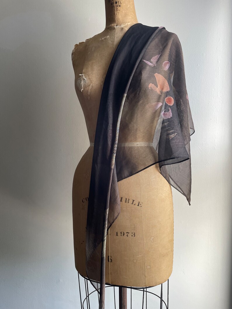 May include: A sheer black scarf with a brown, pink, and white abstract print. The scarf is draped over a dress form.