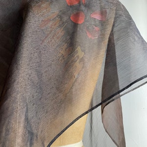 May include: A sheer black scarf with a floral print in shades of red, orange, and purple. The scarf is trimmed with a black border.