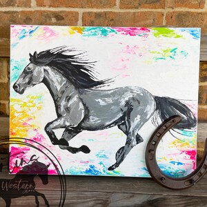 May include: A painting of a gray horse running with a black mane and tail. The background is a colorful abstract design with splashes of pink, blue, green, and yellow. A rusty horseshoe is in the foreground.