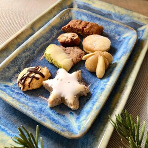 Könnte beinhalten: Ein blauer und weißer Keramikteller mit verschiedenen Weihnachtskeksen. Die Kekse sind mit Zuckerguss, Schokolade und Nüssen verziert.