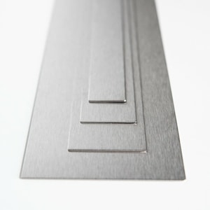 May include: Four different sizes of brushed silver metal sheets stacked on top of each other.