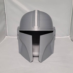 May include: A gray 3D printed helmet with a white stripe down the center. The helmet has a visor and a Mandalorian design.