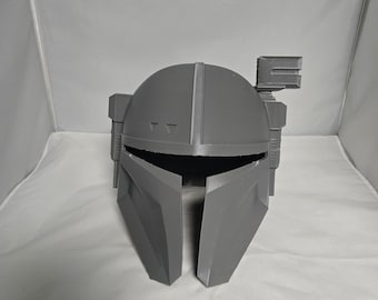 May include: A grey 3D printed helmet with a visor and a small antenna on top. The helmet has a textured surface and a geometric design.