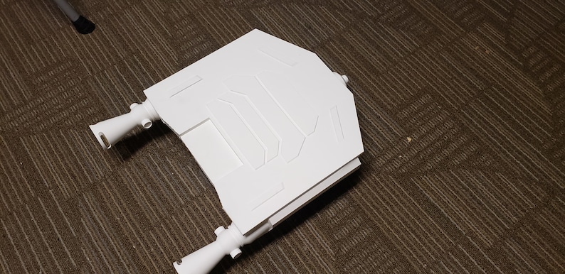 May include: A white, geometric-shaped object with a series of rectangular and angled panels. The object has two cylindrical extensions on either side. The item is made of a solid, opaque material.