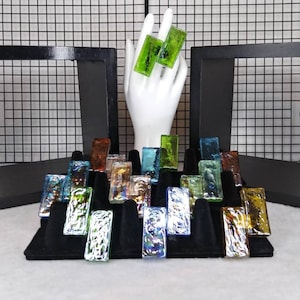 May include: Assortment of colorful glass tiles displayed on a black velvet display stand. The tiles are iridescent and have a variety of shapes and sizes.