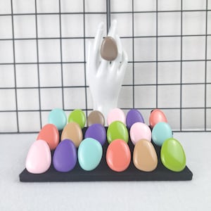 May include: Assortment of colorful oval-shaped rings displayed on a black velvet surface. The rings are in various shades of pink, green, blue, brown, and orange.