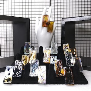May include: A display of iridescent glass rings in various colors, including gold, silver, and blue. The rings are arranged on a black velvet display stand.