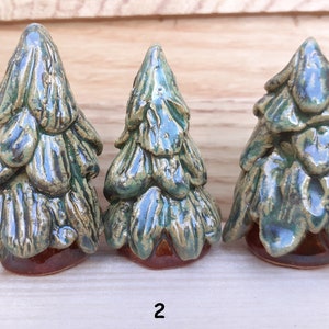 Puede incluir: Tres figuritas de &aacute;rbol de pino de cer&aacute;mica en varios tama&ntilde;os. Los &aacute;rboles son verdes con bases marrones y un acabado esmaltado.