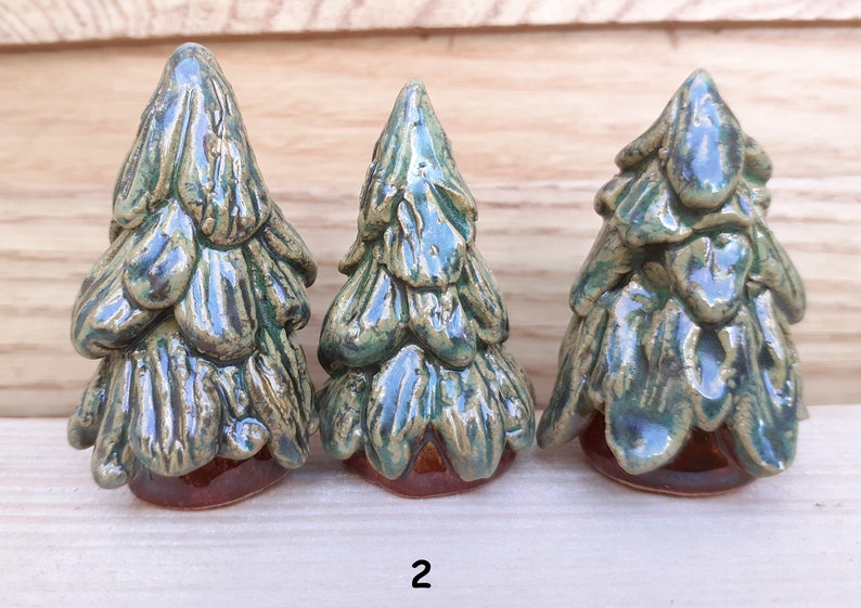 Puede incluir: Tres figuritas de &aacute;rbol de pino de cer&aacute;mica en varios tama&ntilde;os. Los &aacute;rboles son verdes con bases marrones y un acabado esmaltado.
