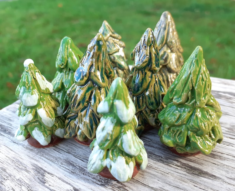 Puede incluir: Una colecci&oacute;n de ocho peque&ntilde;os &aacute;rboles de Navidad de cer&aacute;mica en varios tonos de verde con detalles blancos. Los &aacute;rboles est&aacute;n dispuestos sobre una superficie de madera.