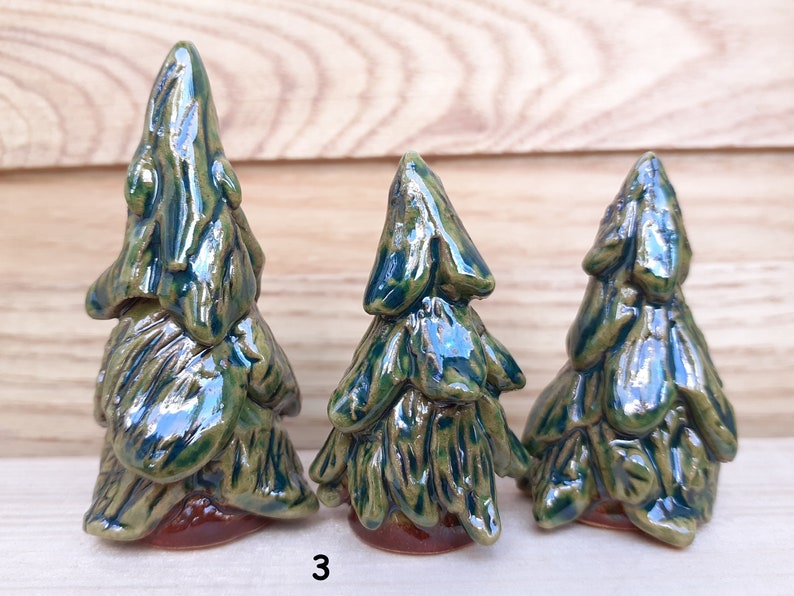 Puede incluir: Tres &aacute;rboles de pino de cer&aacute;mica de diferentes tama&ntilde;os, con un esmalte verde y marr&oacute;n. Los &aacute;rboles est&aacute;n dispuestos de mayor a menor, con el &aacute;rbol m&aacute;s grande a la izquierda y el m&aacute;s peque&ntilde;o a la derecha. Los &aacute;rboles est&aacute;n todos sobre una superficie de madera. El n&uacute;mero "3" est&aacute; escrito en la superficie delante de los &aacute;rboles.