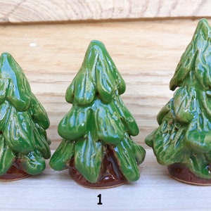 Puede incluir: Tres figuritas de &aacute;rbol de pino de cer&aacute;mica en diferentes tama&ntilde;os. Los &aacute;rboles son verdes con bases marrones. Los &aacute;rboles est&aacute;n dispuestos en orden de tama&ntilde;o de izquierda a derecha.