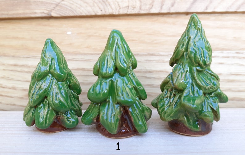 Puede incluir: Tres figuritas de &aacute;rbol de pino de cer&aacute;mica en diferentes tama&ntilde;os. Los &aacute;rboles son verdes con bases marrones. Los &aacute;rboles est&aacute;n dispuestos en orden de tama&ntilde;o de izquierda a derecha.