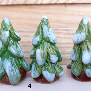 Puede incluir: Tres peque&ntilde;os &aacute;rboles de Navidad de cer&aacute;mica pintados en verde y blanco, cada uno con una base marr&oacute;n. Los &aacute;rboles est&aacute;n decorados con acentos blancos que parecen nieve.