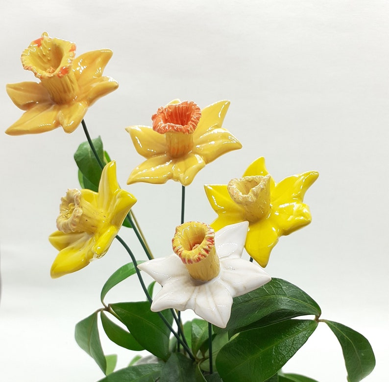 May include: A bouquet of five ceramic daffodils in a variety of colors, including yellow, white, and orange. The flowers are arranged in a vase with green leaves.