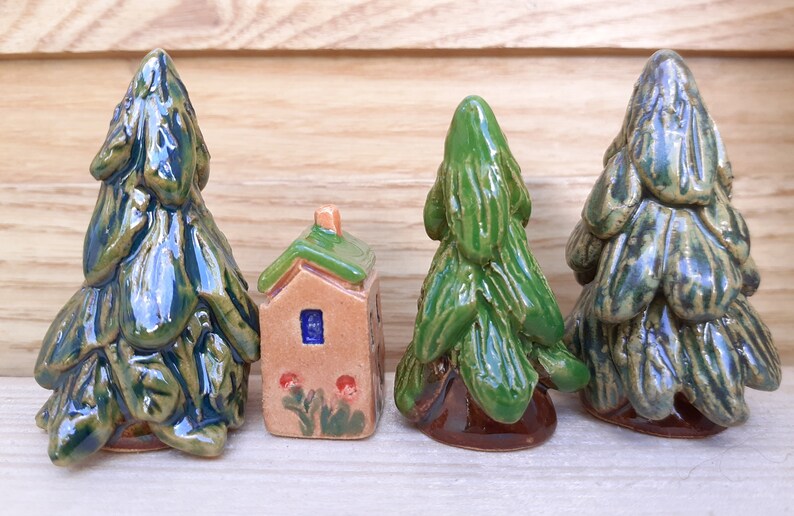 Puede incluir: Cuatro figuritas de cer&aacute;mica, tres &aacute;rboles verdes y una peque&ntilde;a casa marr&oacute;n con techo verde y ventana azul. Las figuritas est&aacute;n pintadas a mano y tienen un aspecto r&uacute;stico y vintage.