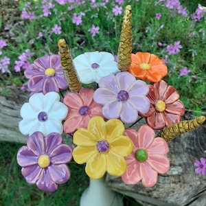 Op de afbeelding: Een keramisch bloemboeket in een witte vaas. Het boeket bevat kleurrijke bloemen in tinten paars, oranje, roze, geel en wit. De bloemcentra hebben een contrasterende kleur. De stelen zijn goudkleurig getextureerd.