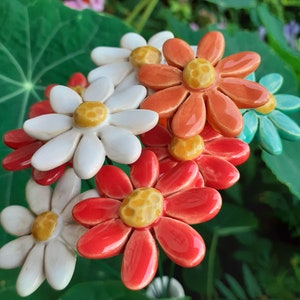 Può includere: Un bouquet di fiori in ceramica in tonalità di bianco, rosso, arancione e turchese. I fiori hanno centri gialli e sono disposti in un grappolo.