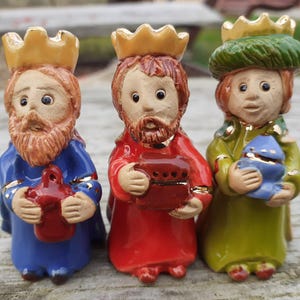 Op de afbeelding: Drie keramische beeldjes van de Drie Wijzen, elk met een gouden kroon en een geschenk. De figuren dragen blauwe, rode en groene gewaden met gouden accenten. De beeldjes zijn ongeveer 10 cm hoog.