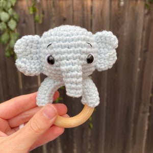 Op de afbeelding: Een lichtblauwe gehaakte olifantenrammelaar met zwarte ogen en een houten ring.
