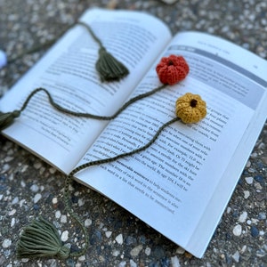 May include: A close-up of a book with a green and brown bookmark with tassels. The bookmark has crocheted flowers attached to it. The book is open to a page with text about memory techniques.